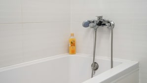 Uma banheira branca com um chuveiro manual e uma garrafa de shampoo.