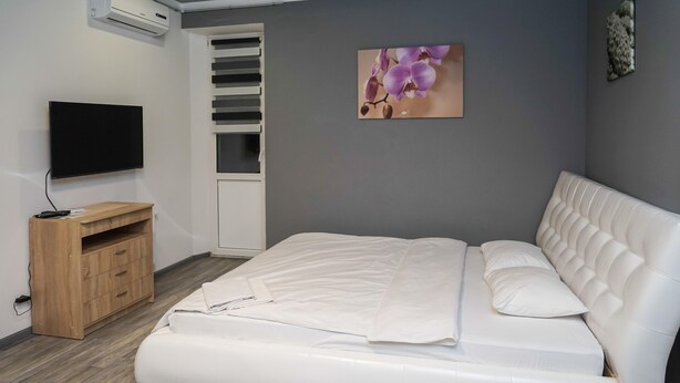 Um quarto com uma cama, televisão, cómoda de madeira e guarda-roupa com porta deslizante.