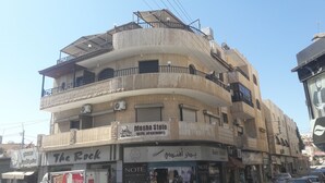 A multi-story building with balconies, air conditioning units, and various signs including "Mesha Stele Hotel Apartments" and "The Rock". - Mesha Stele Hotel Apartments (Madaba)