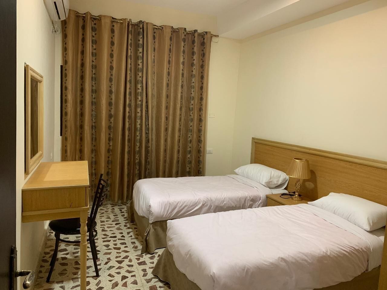 A hotel room with two beds, a desk, a chair, and a window with curtains.