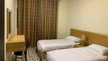 Une chambre d’hôtel avec deux lits, un bureau, une chaise et une fenêtre avec des rideaux.
