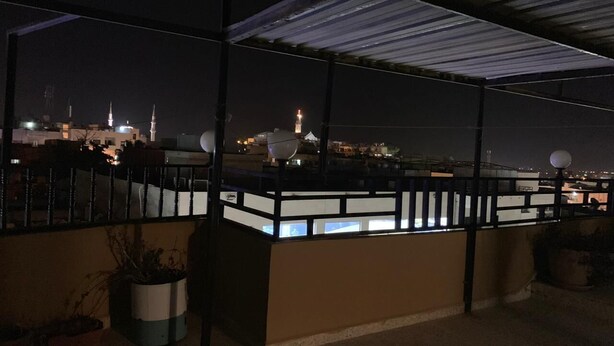 A rooftop terrace with a view of a city skyline at night, including a prominent tower. - Mesha Stele Hotel Apartments (Madaba)