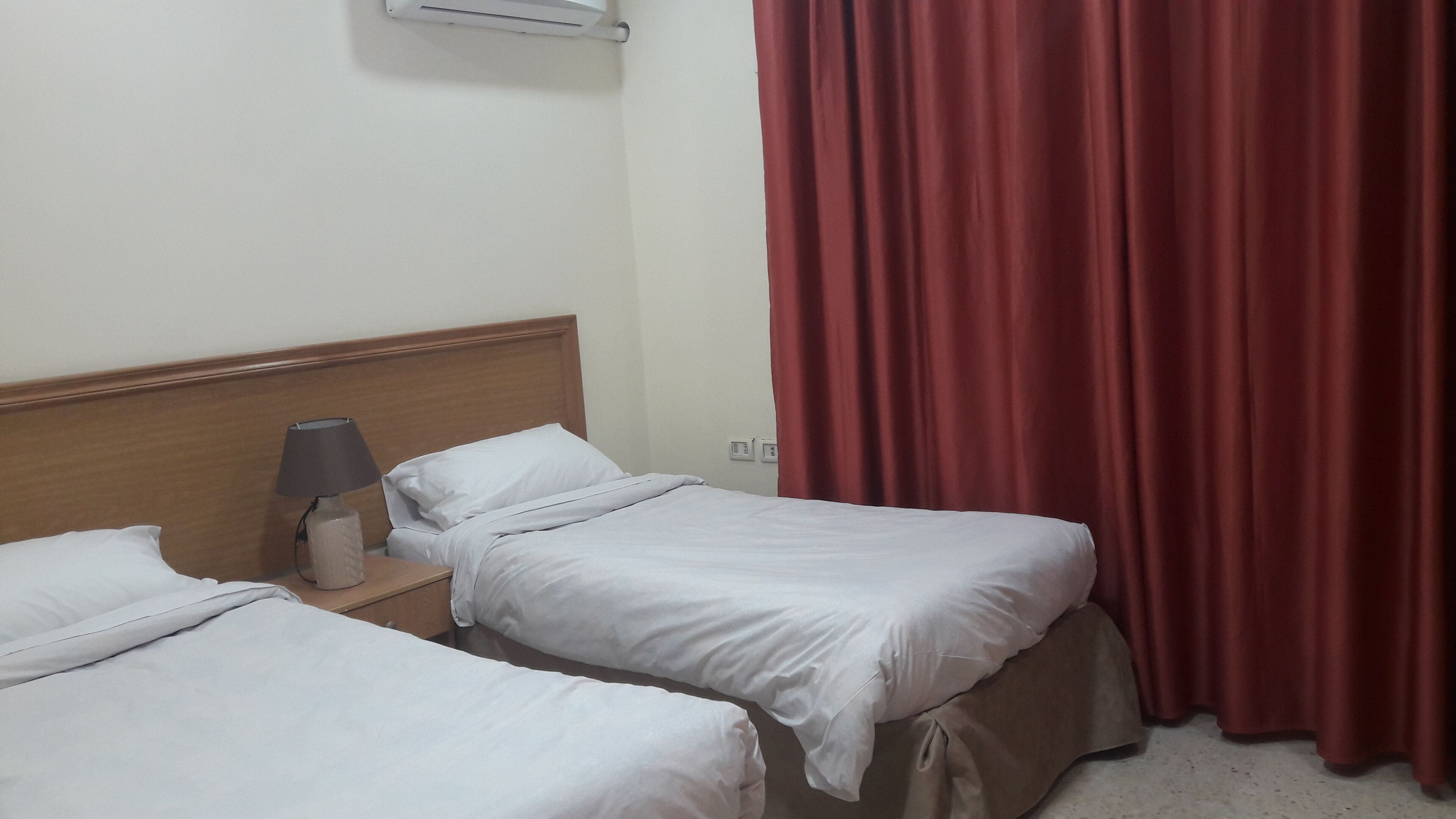 Una habitación de hotel con dos camas individuales, una mesita de noche con lámpara y una cortina roja.