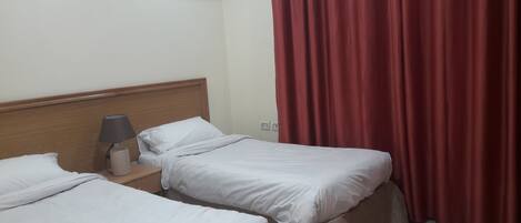 Una habitación de hotel con dos camas individuales, una mesita de noche con lámpara y una cortina roja.