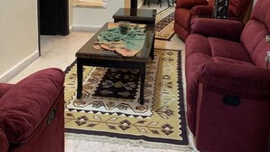 A living room with a sofa, armchairs, a coffee table, and a dining area with chairs and a table. - Mesha Stele Hotel Apartments (Madaba)
