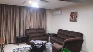 A living room with two brown sofas, a small table, a radiator, and a patterned rug. - Mesha Stele Hotel Apartments (Madaba)
