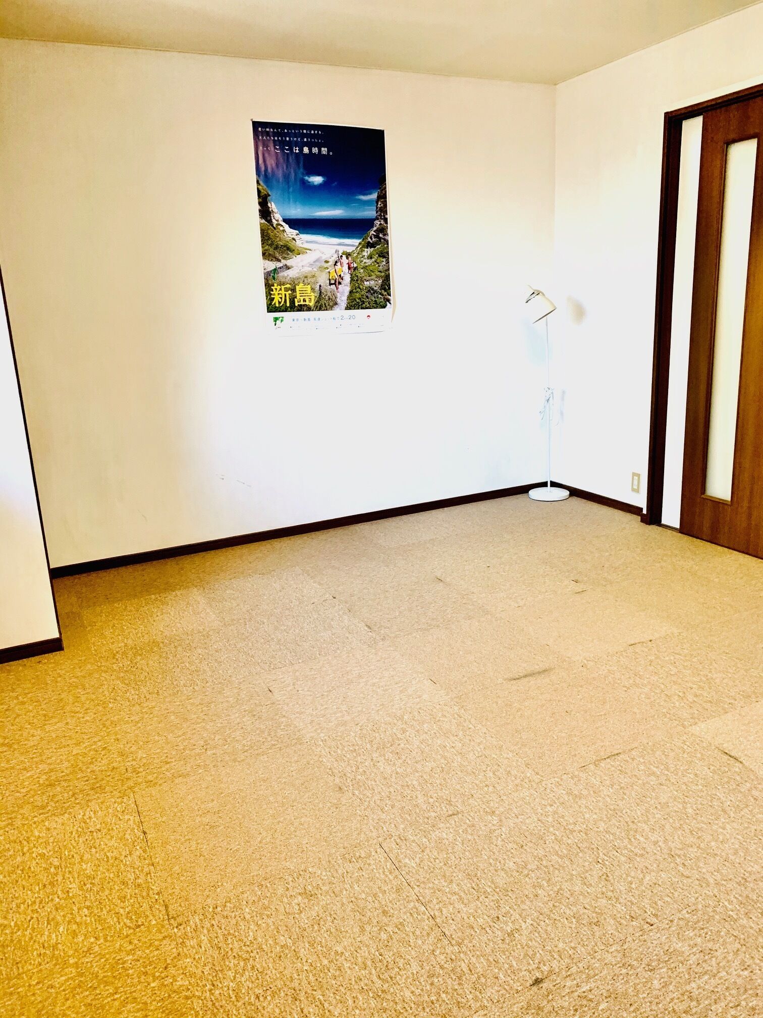 Una habitación con alfombra color beige, un cartel en la pared y una puerta de madera.