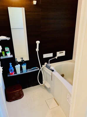 A modern bathroom with a bathtub, a shower, and a vanity with toiletries. - Guesthouse IKETA (Niijima)