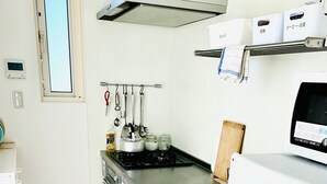 A compact kitchen with white cabinets, a stainless steel sink, and a built-in stove. There is a small refrigerator and a microwave on the countertop. - Guesthouse IKETA (Niijima)