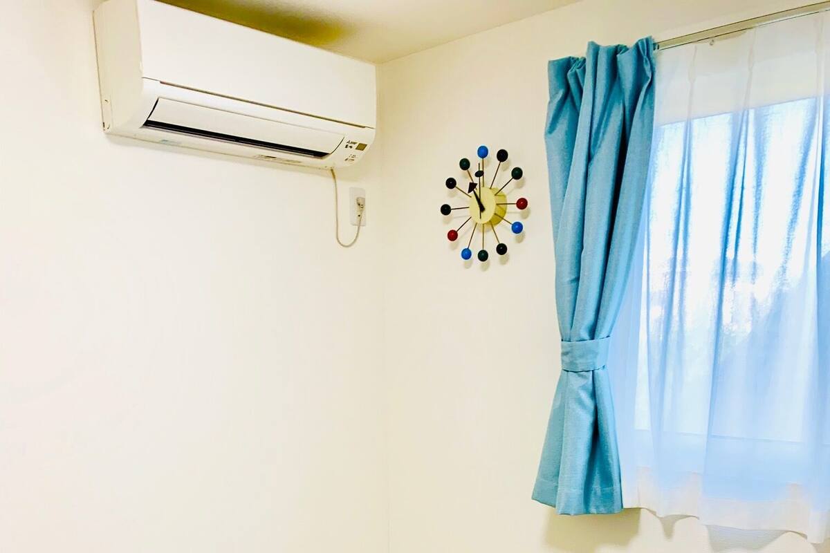 A room with a beige carpet, a white air conditioning unit, a blue curtain, and a wall clock.