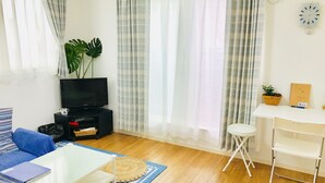 A living room with a TV, sofa, coffee table, and a small white table with a plant and notebook. - Guesthouse IKETA (Niijima)