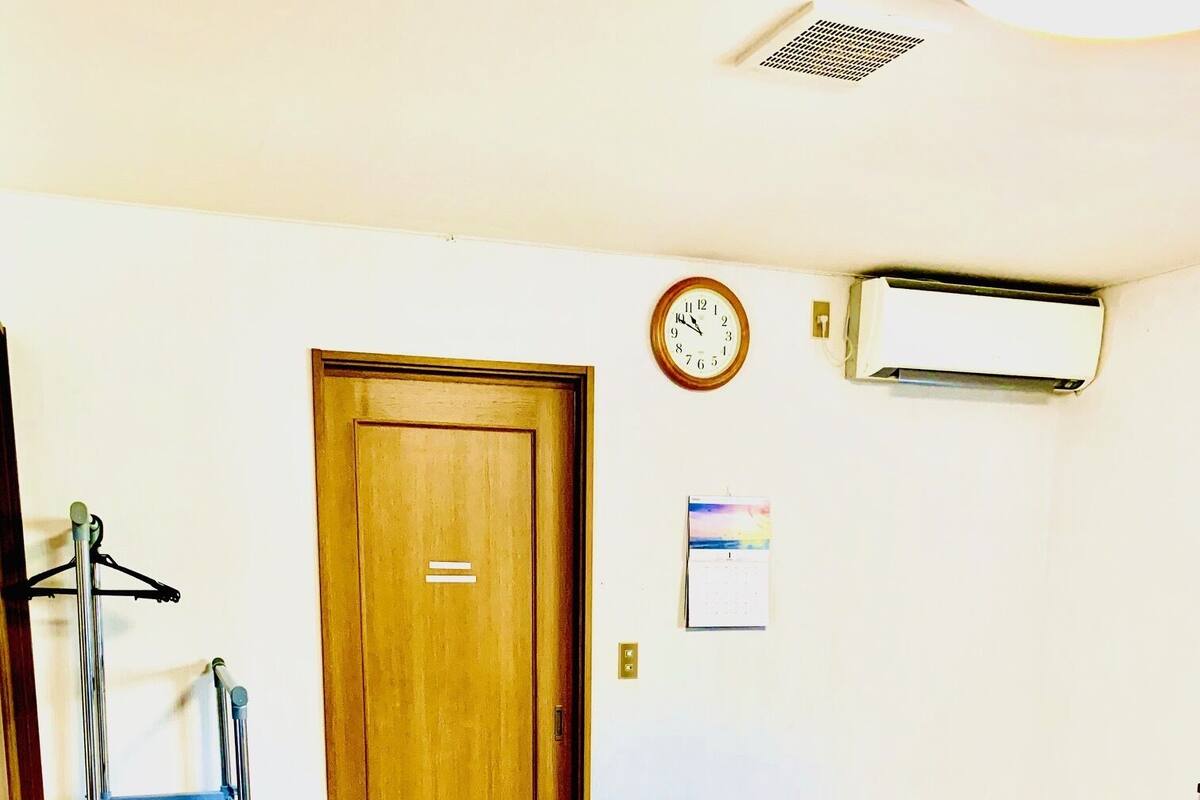 A room with a wooden door, a wall-mounted air conditioner, a calendar, and a metal ladder.