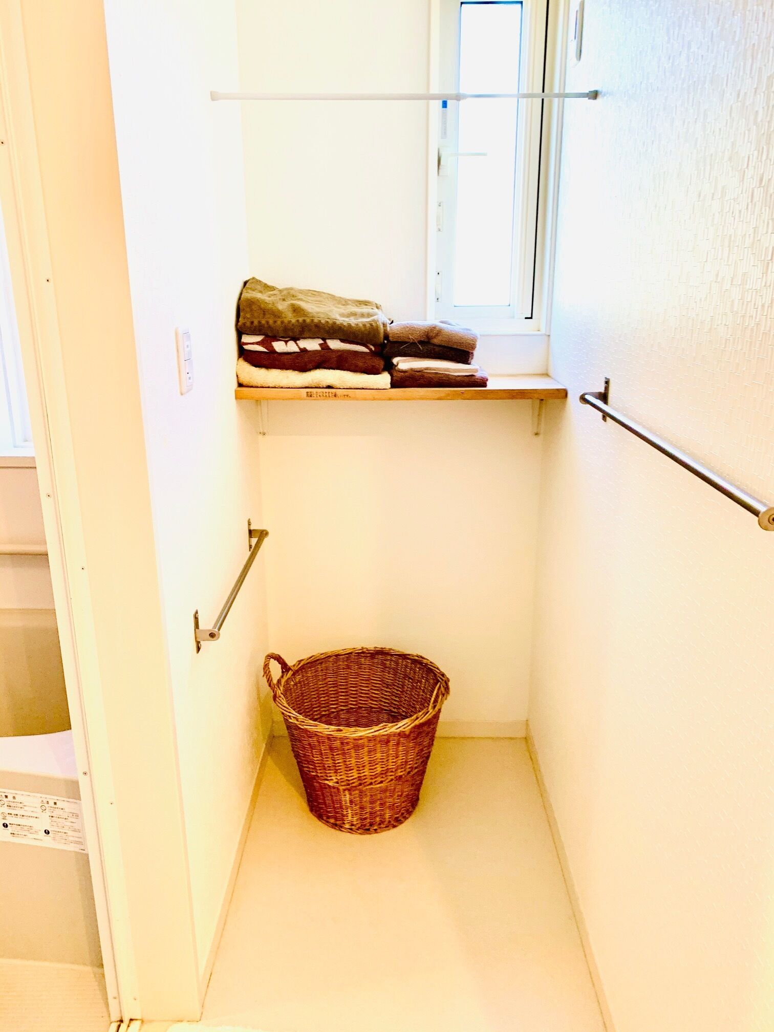 A narrow hallway with a wooden shelf holding folded blankets, a wicker basket, and a handrail on the right.