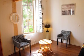 Une pièce avec deux fauteuils à motifs, une table ronde et une fenêtre avec des rideaux.