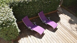 Dos sillones morados en una terraza de madera con un seto al fondo.