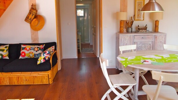 Una sala de estar acogedora con un sofá, cojines coloridos, una mesa de comedor con sillas y un mueble de madera.