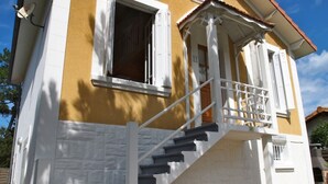 Un edificio de dos plantas con fachada blanca y amarilla, un balcón con barandillas blancas y una escalera que lleva al segundo piso.