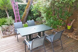 An outdoor patio with a table and chairs, surrounded by greenery and a wooden deck.