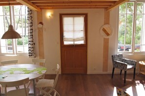 Une pièce avec une porte en bois, une table ronde entourée de chaises et de grandes fenêtres avec des rideaux.