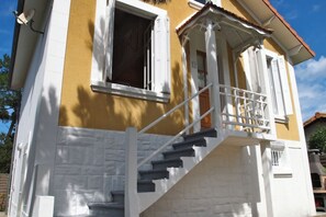 Un immeuble de deux étages avec une façade blanche et jaune, un balcon doté d’une balustrade blanche, et le numéro « 21 » bien visible sur le bâtiment.