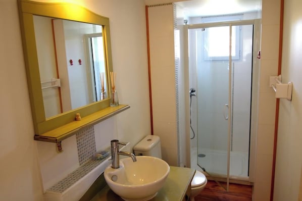 A bathroom with a sink, mirror, toilet, and glass-enclosed shower.