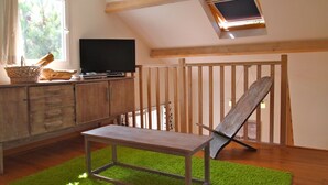 Una habitación con un banco de madera, un televisor sobre un mueble y una ventana que da a árboles.