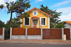 A yellow house with a red roof, white window frames, and a wooden fence.
