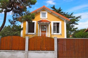 A yellow house with a red roof, white trim, and a wooden fence.