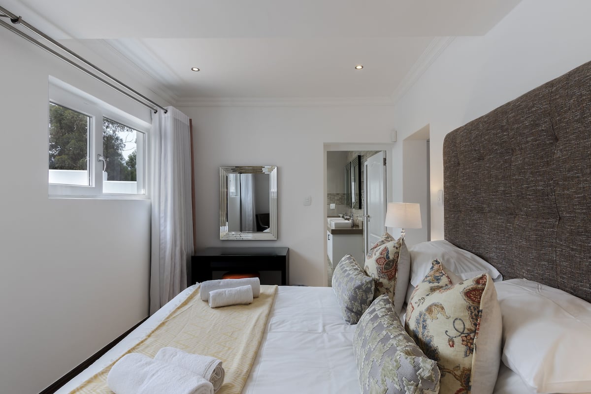 Habitación de hotel moderna con una cama grande, una mesita de noche, un espejo y vistas al exterior.