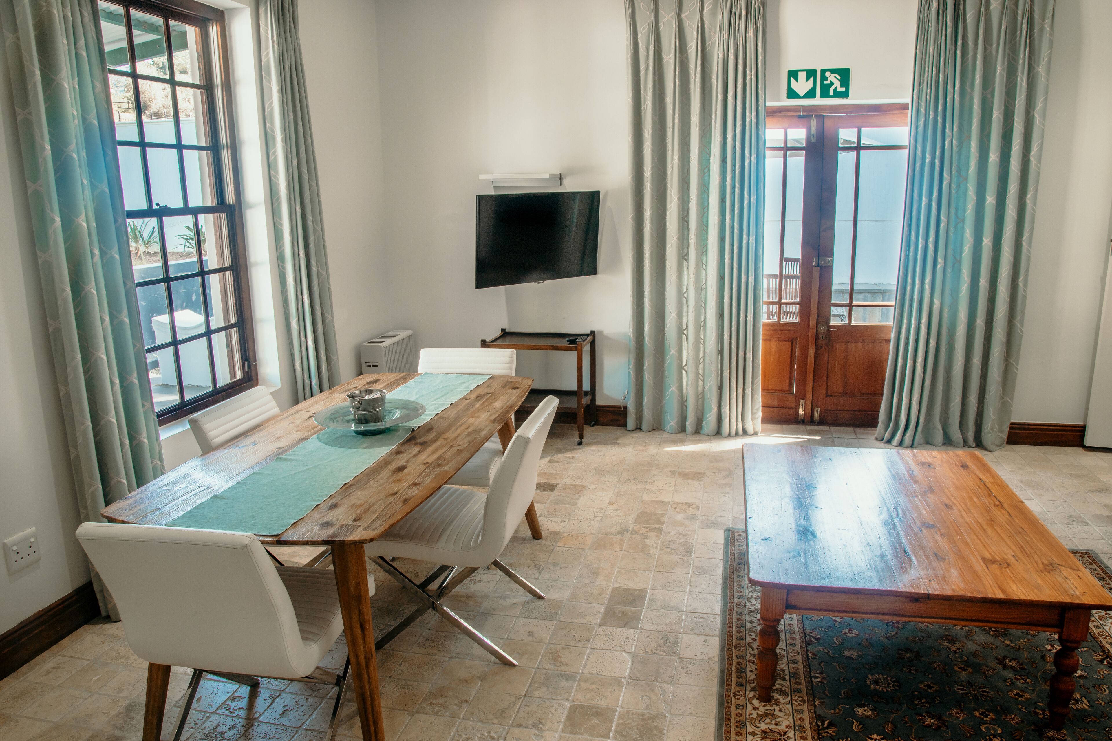 Hotelkamer met een houten eettafel, witte stoelen, een flatscreen tv aan de muur en uitzicht op het landschap door een groot raam.