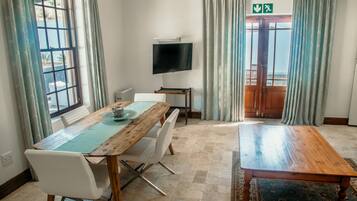 Hotelkamer met een houten eettafel, witte stoelen, een flatscreen tv aan de muur en uitzicht op het landschap door een groot raam.