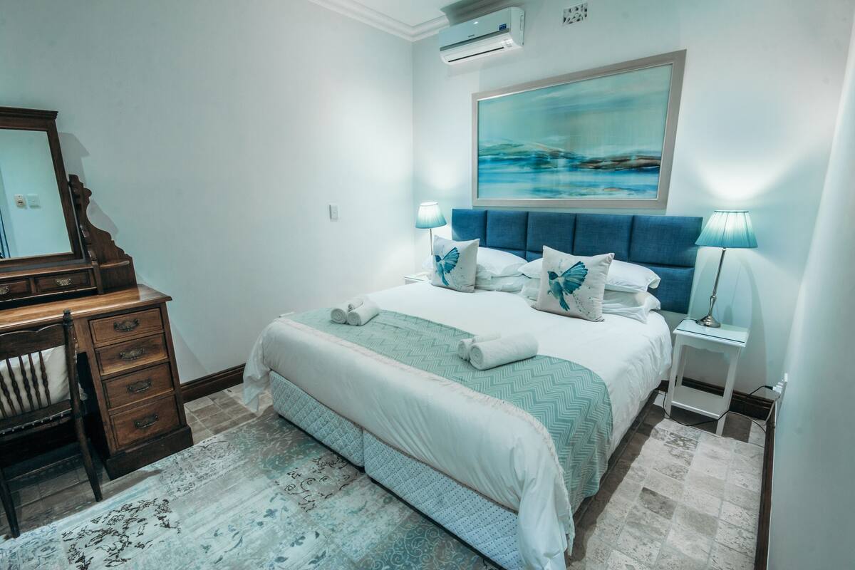 Un dormitorio con cama, mesitas de noche, cómoda y un cuadro en la pared.