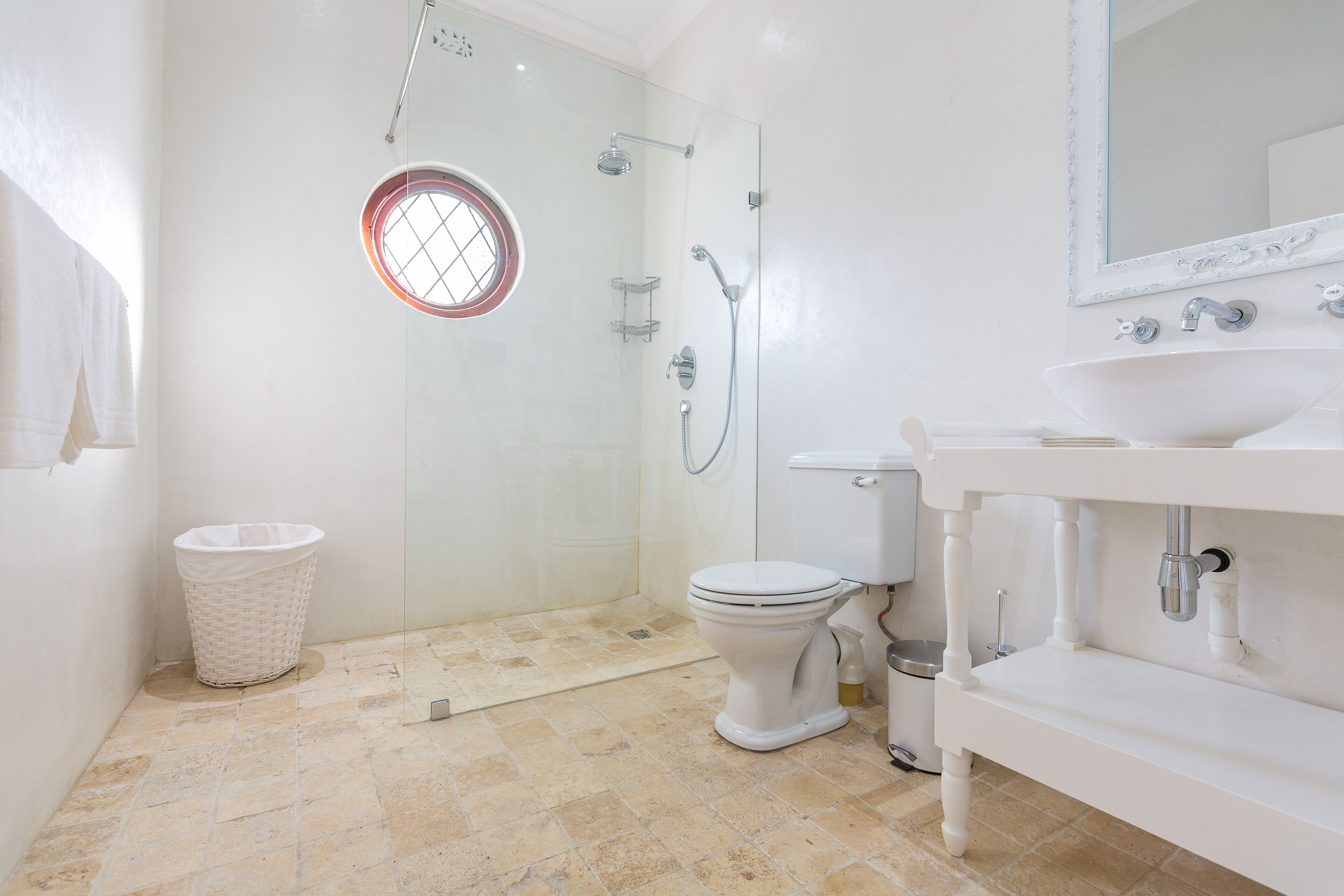 A bathroom with a glass-enclosed shower, a white toilet, a sink, and a round window.