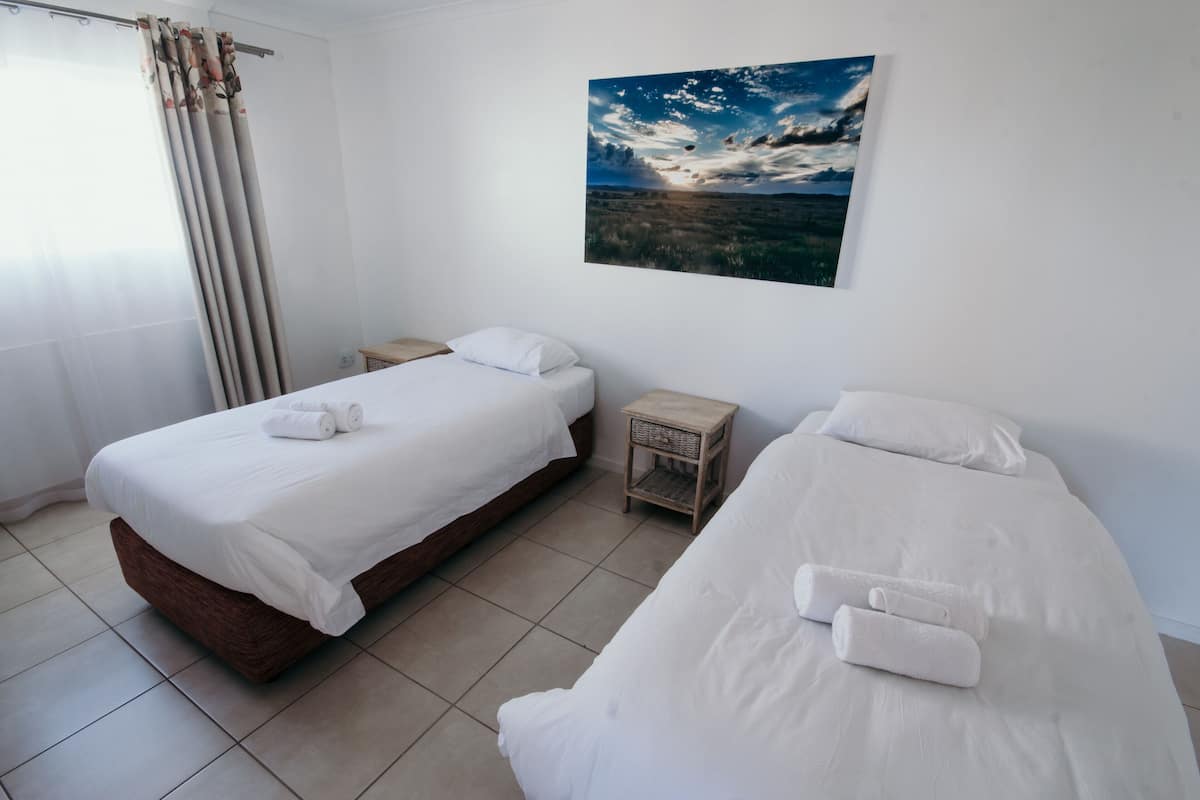 Habitación de hotel con dos camas, una mesita de noche de madera y un cuadro de paisaje colgado en la pared.