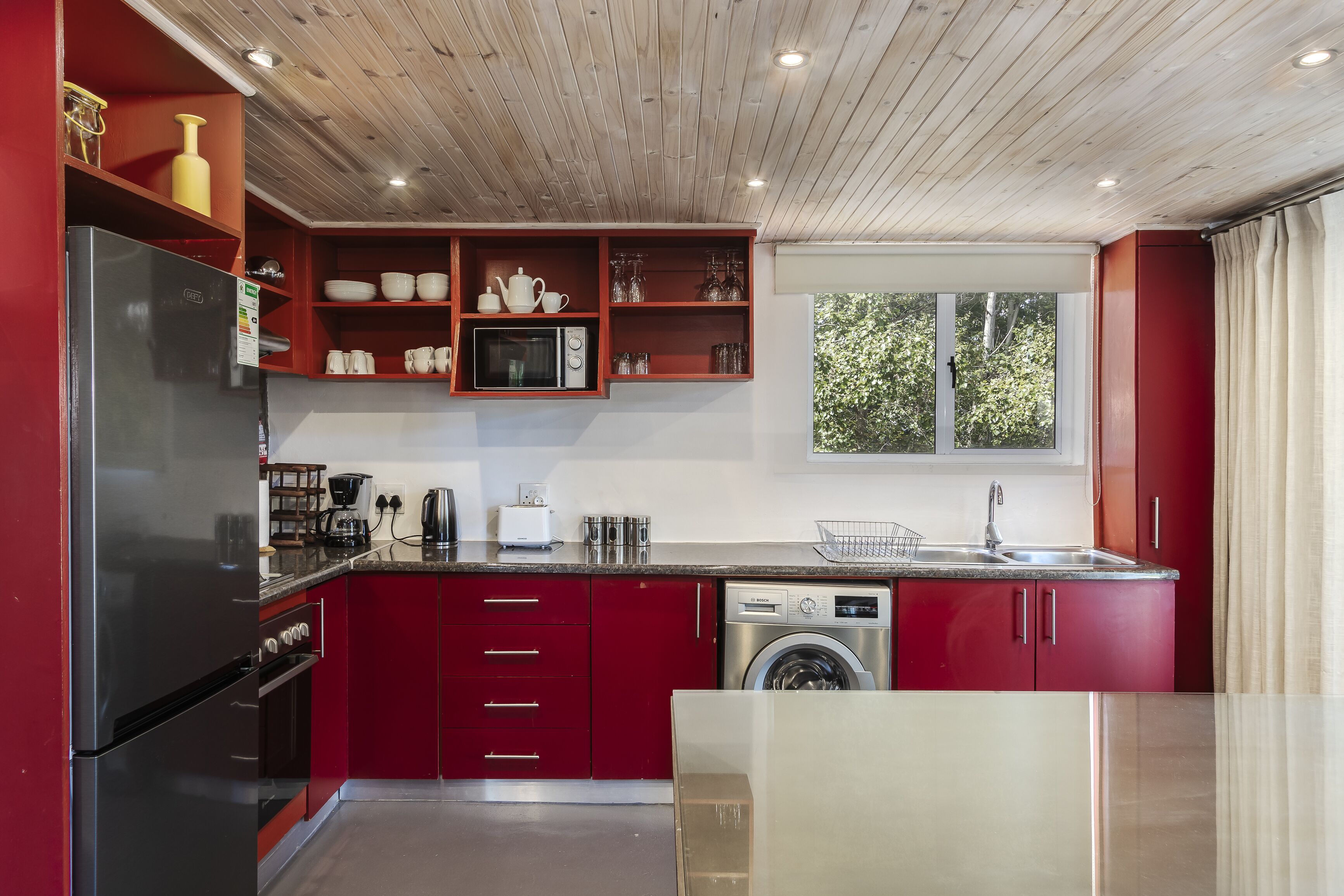Una cucina moderna con mobili rossi, elettrodomestici in acciaio inossidabile e una finestra che lascia entrare luce naturale.