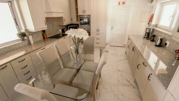 A modern kitchen with white cabinetry, a marble countertop, and a dining area with a glass table and chairs.