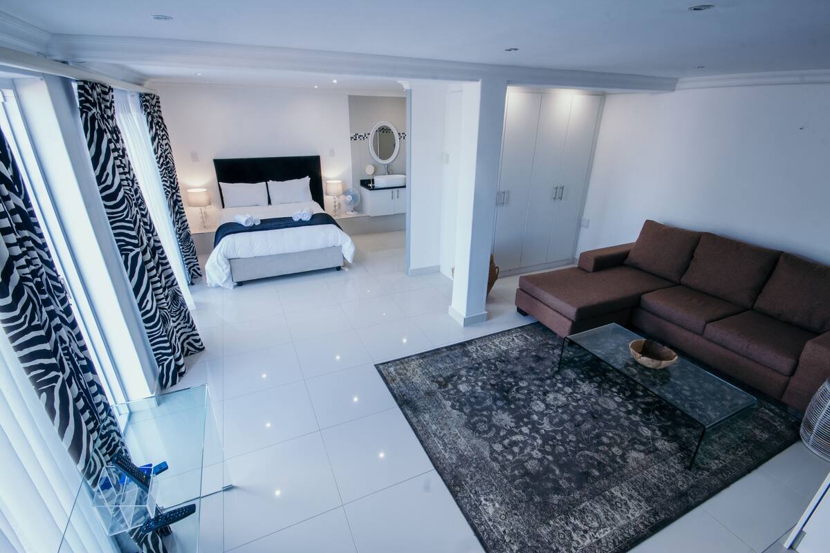 Una habitación de hotel moderna con una cama, un sofá marrón, una mesa de centro de cristal y una cortina con estampado de cebra.