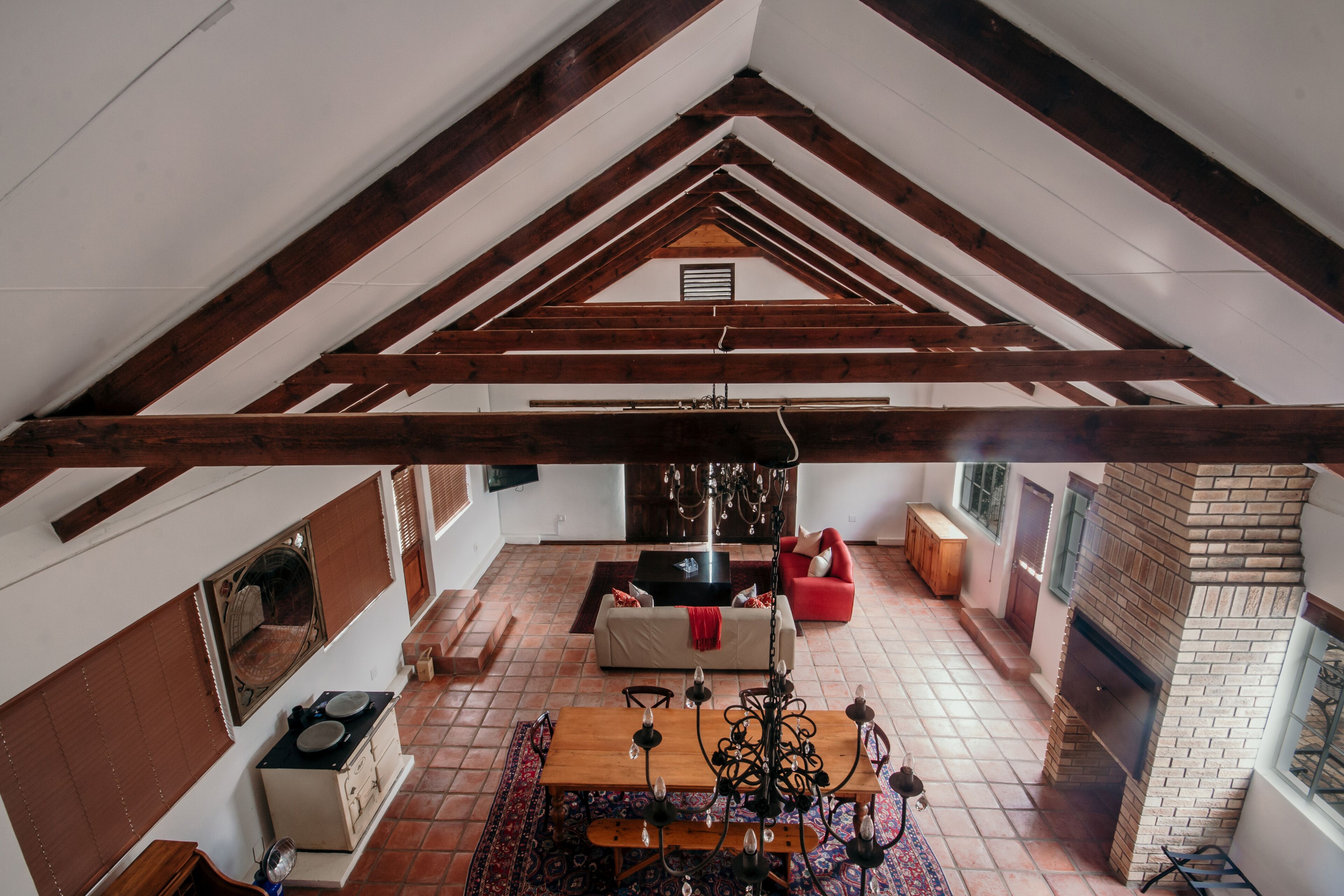 A spacious loft with exposed wooden beams, a fireplace, a dining area with a chandelier, and a cozy seating area.