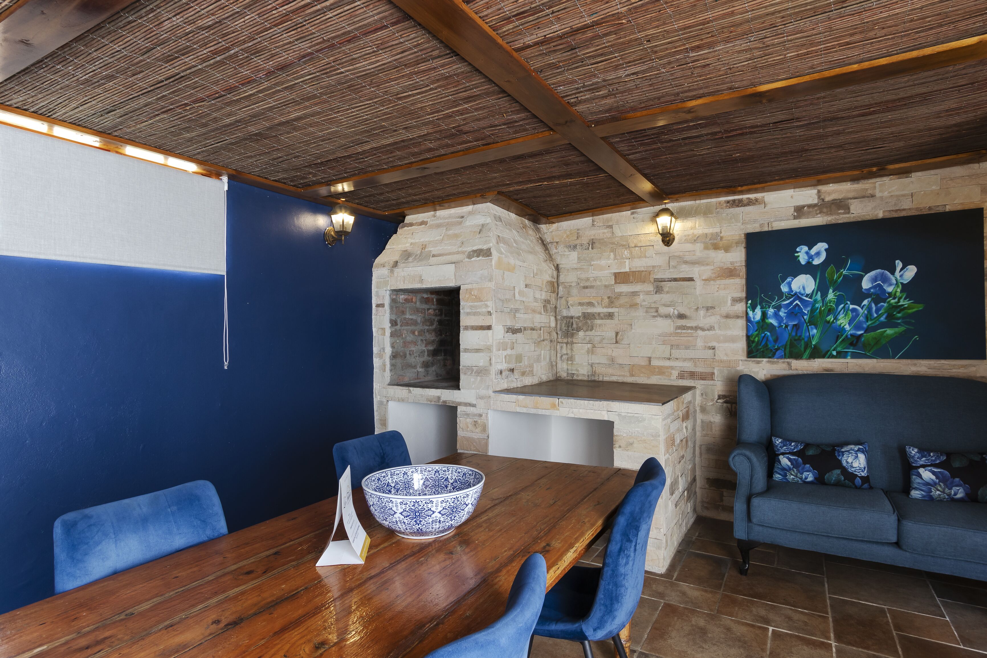 Un comedor con mesa de madera, sillas azules, chimenea de piedra y pared azul.
