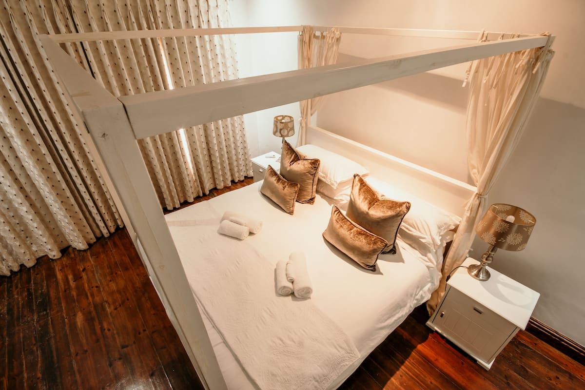 Una cama individual con dosel, ropa de cama blanca y almohadas decorativas.