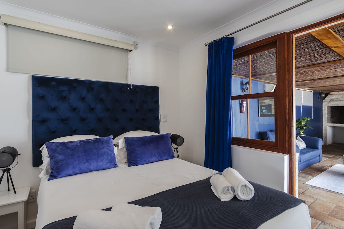 Habitación de hotel con una cama grande, cabecera azul y vista al área exterior.