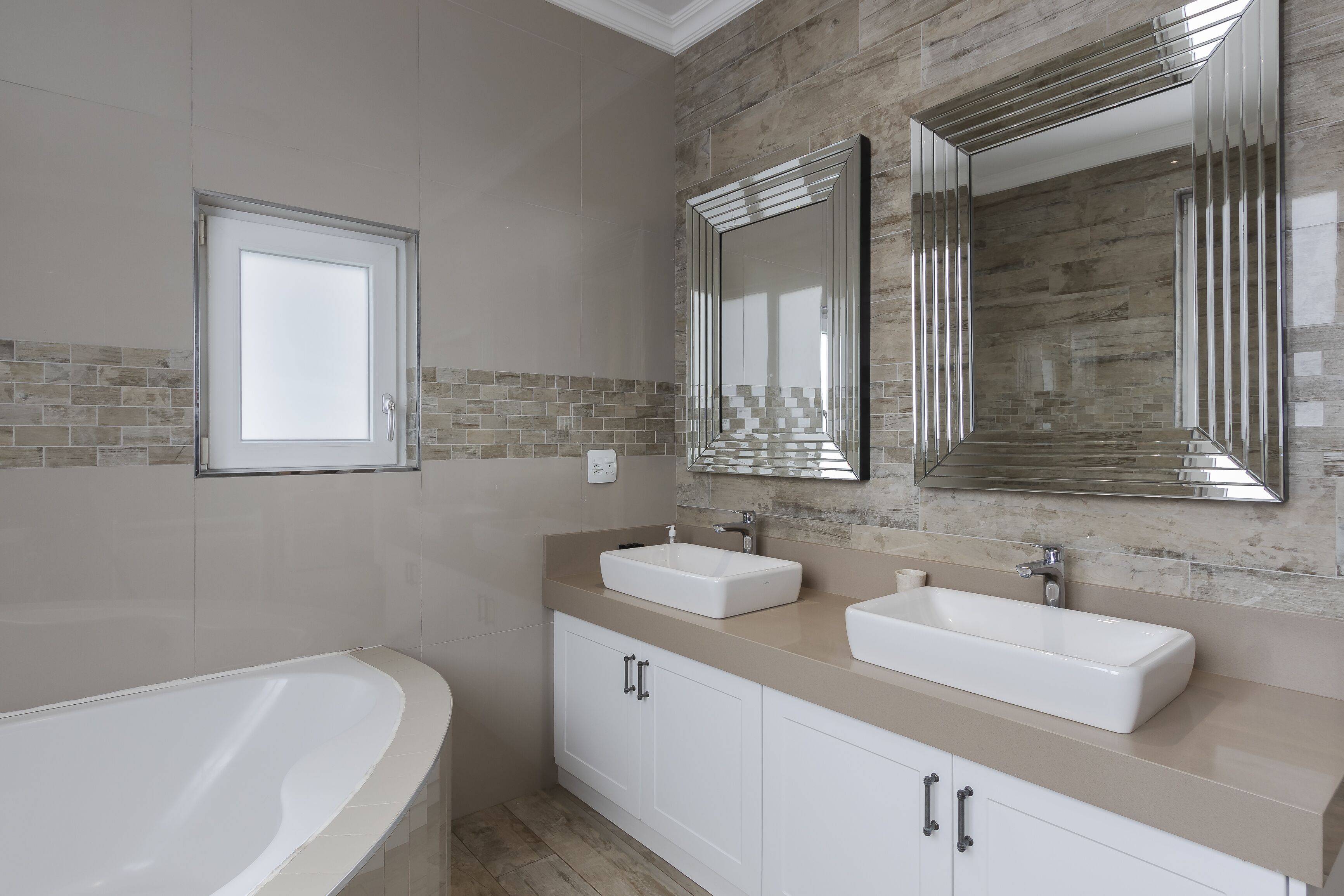 Un baño moderno con dos lavamanos, un espejo grande y una bañera.