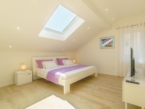 A bedroom with a skylight, a bed with a purple blanket, a bedside table with a lamp, and a TV on a desk. - Dalmat Apartments (Split)