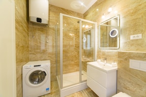 A modern bathroom with a glass-enclosed shower, a built-in washing machine, and a vanity with a mirror. - Dalmat Apartments (Split)