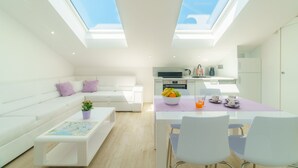 Un espacio habitable moderno con un sofá blanco, una mesa de centro con un mapa, una zona de comedor con una mesa y sillas, y una cocina al fondo.