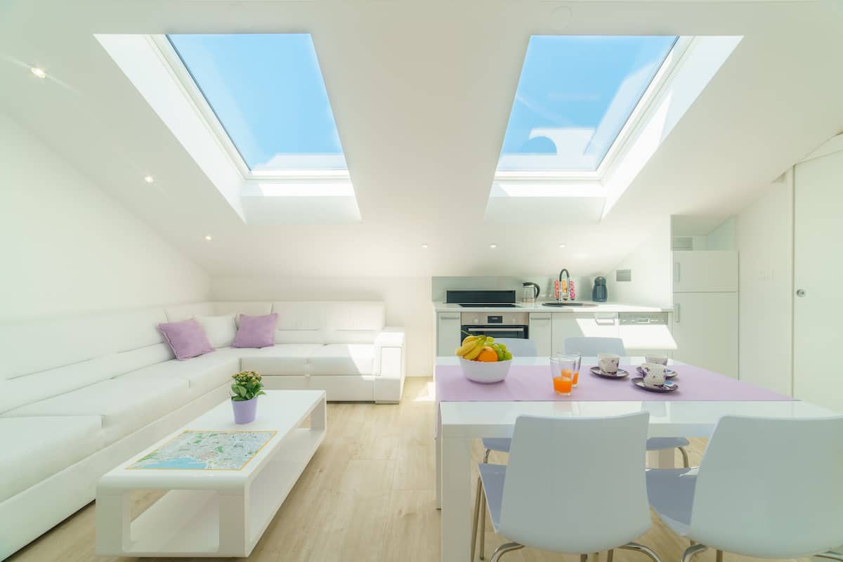 Un espace de vie moderne avec un canapé blanc, une table basse ornée d’une carte, un coin repas avec une table et des chaises, et une cuisine en arrière-plan.