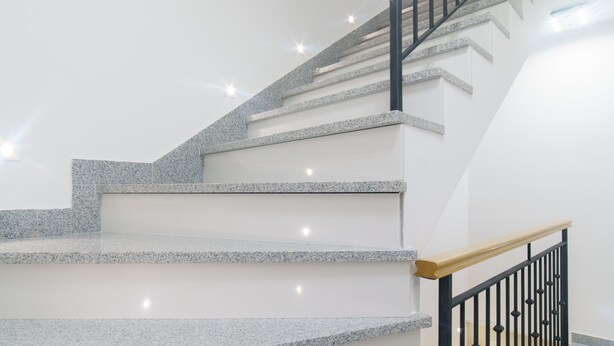 Una escalera con escalones de granito y barandillas negras, que conduce a un piso superior.