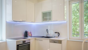 Cocina moderna con armarios blancos, horno empotrado, lavavajillas y ventana con vistas a zonas verdes.