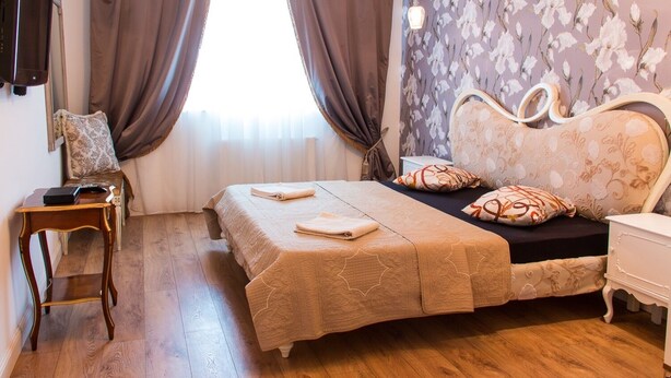 A bedroom with a bed, a bedside table, a lamp, and a window with curtains.