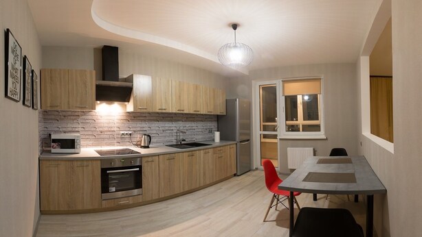 A modern kitchen with wooden cabinets, a built-in oven, and a microwave. There is a dining area with a table and chairs.